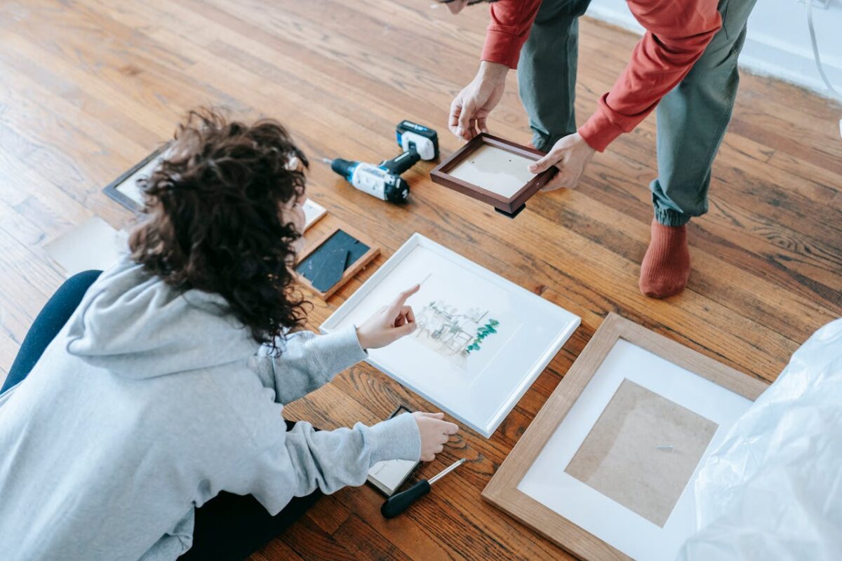 A couple organizing picture frames on a wooden floor, preparing for interior decoration or renovation.
